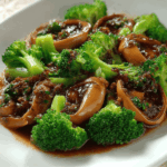 Braised abalone slices with bright green broccoli in a rich sauce, captured with soft lighting.